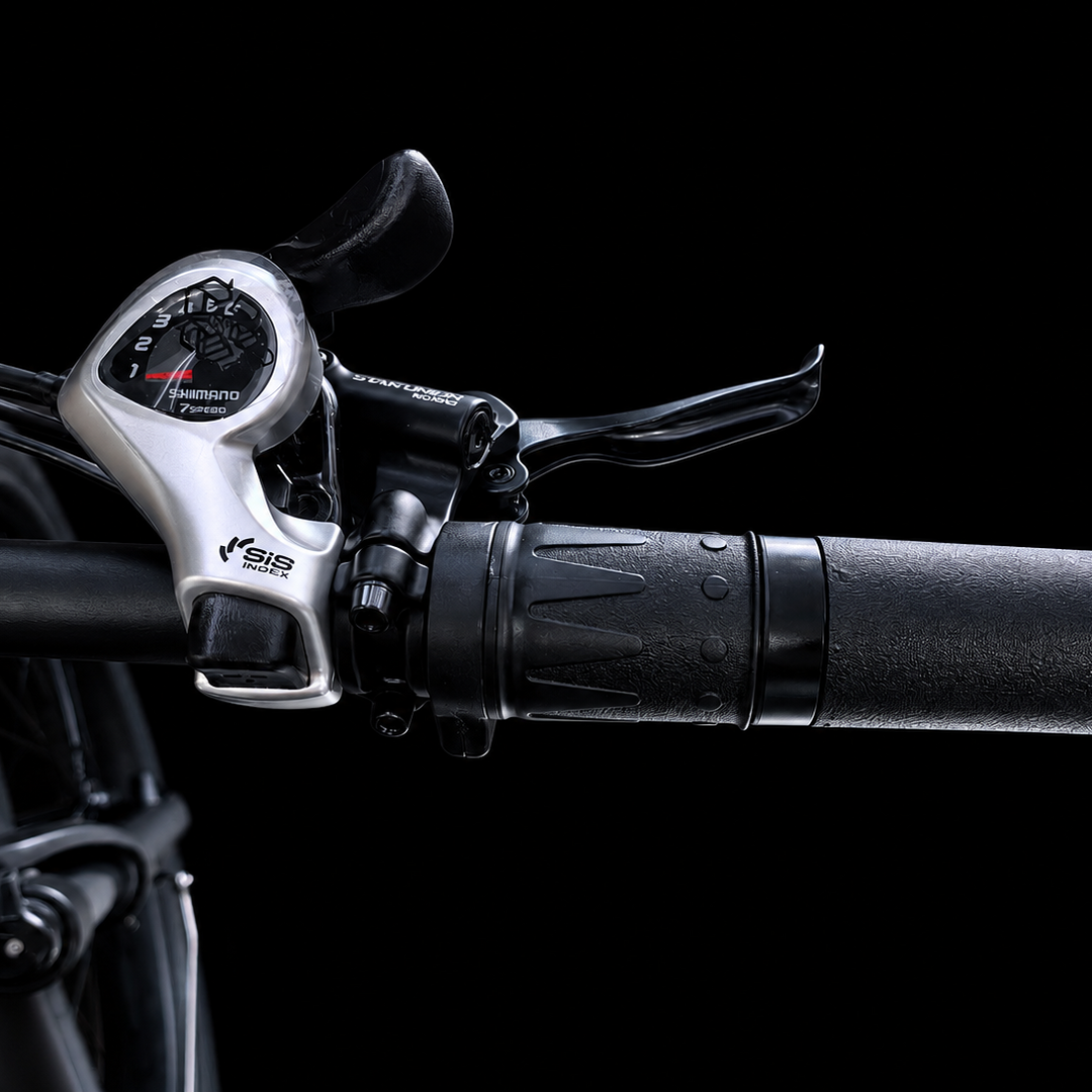 Close-up of a bicycle handlebar with a black textured grip, black lever, and a silver Shimano shifter cluster against a black background.